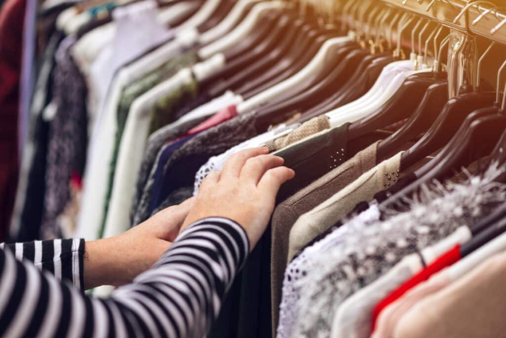 Woman browsing through clothing at second hand street market, selective focus on clothes. Black Friday deals. 